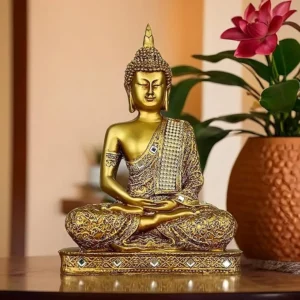 Golden meditating Buddha statue with ornate detailing and jewel-studded robe, placed indoors beside a flower pot, symbolizing peace and mindfulness.